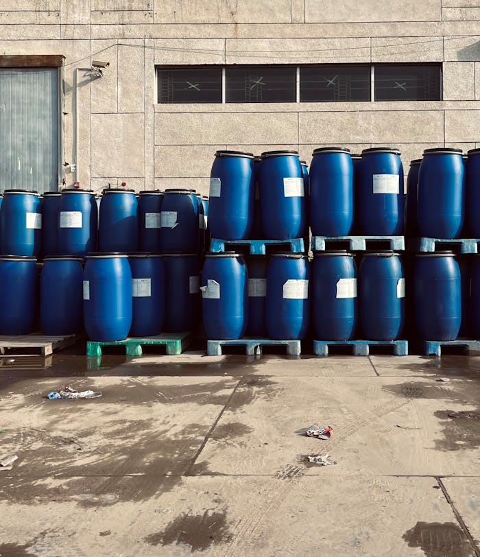Rows of blue industrial barrels stacked on pallets outside a warehouse.