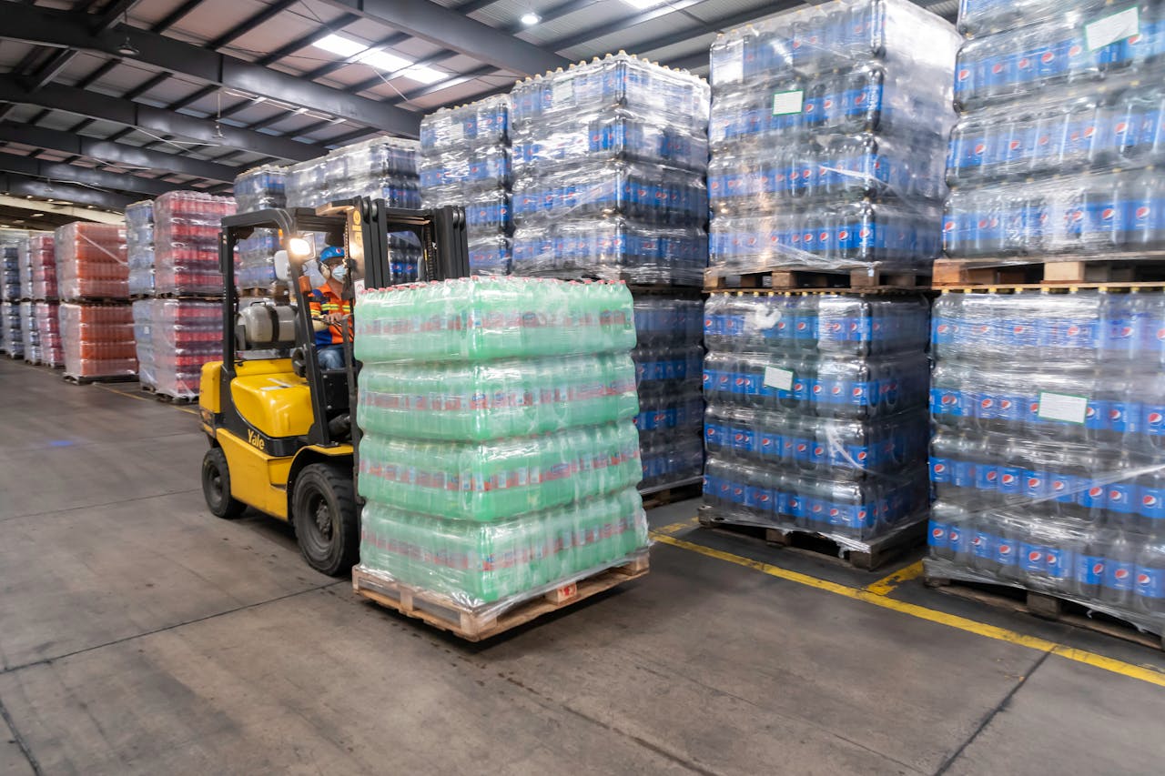 A forklift operator moves stacked pallets in a busy warehouse setting.